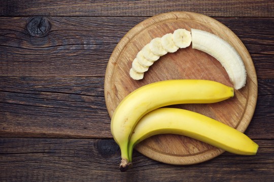 Ripe bananas and a sliced on wooden cutting board, top view