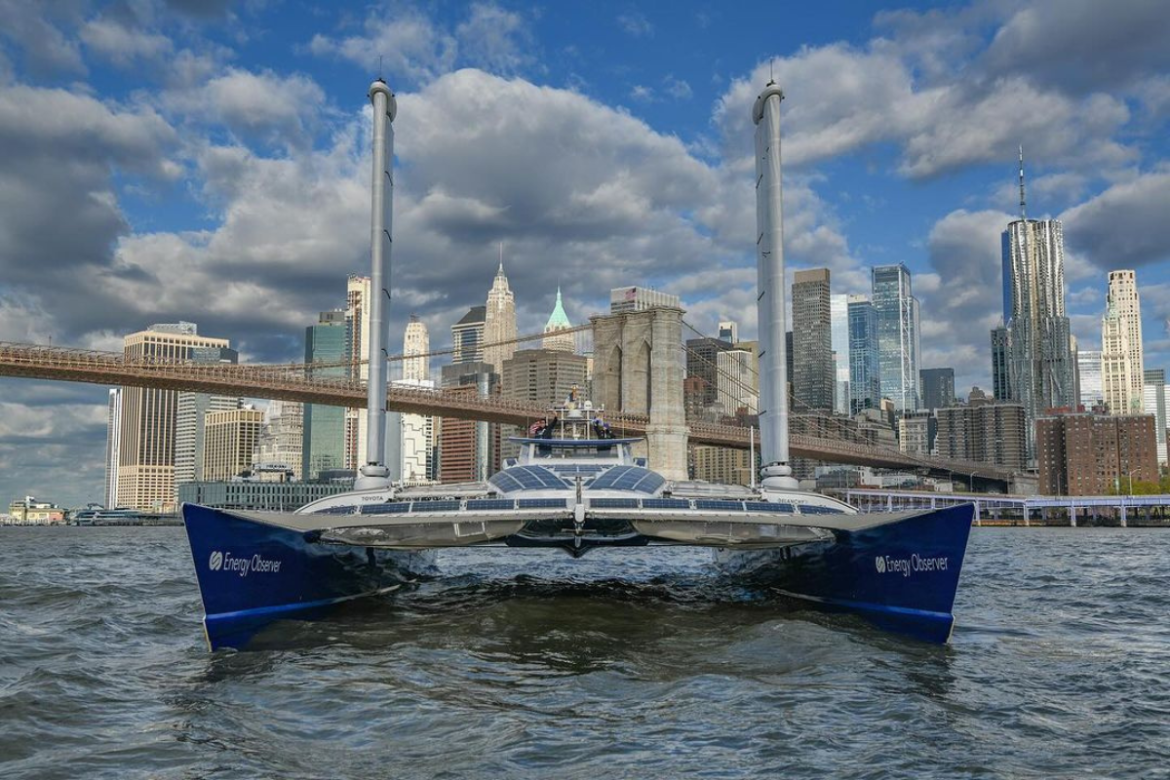 Energy Observer Boat in the Water with NYC and the Brooklyn Bridge int he background.