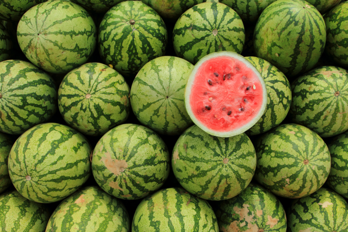 A pile of whole watermelons, with one melon cut in half on top.