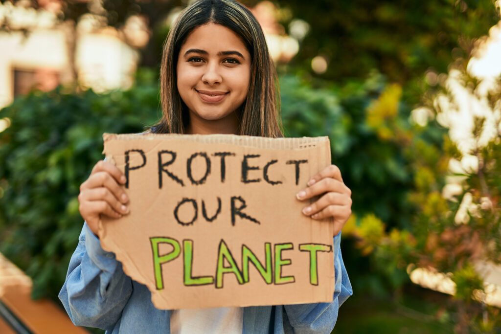 Young smiling woman in a park holding a sign that reads "Protect Our Planet".